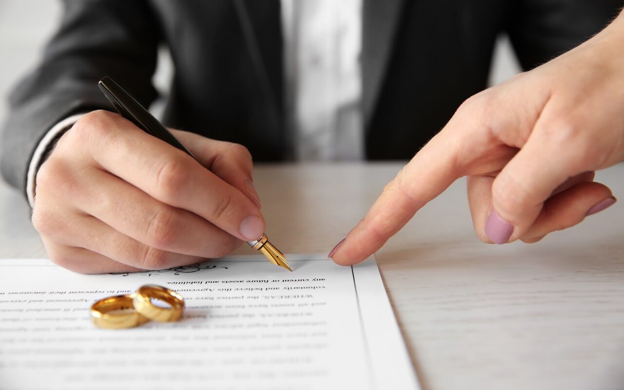Hand signing divorce with wedding rings